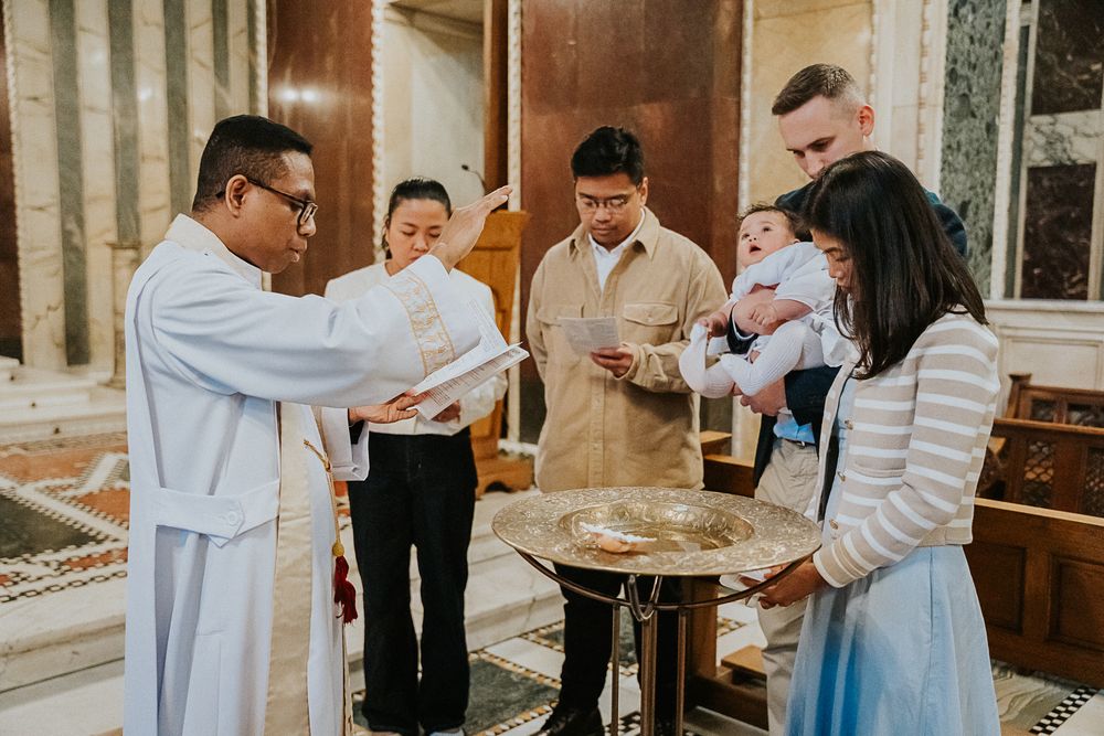 A baptismal ceremony takes place with people gathered around a baptismal font in a church.
