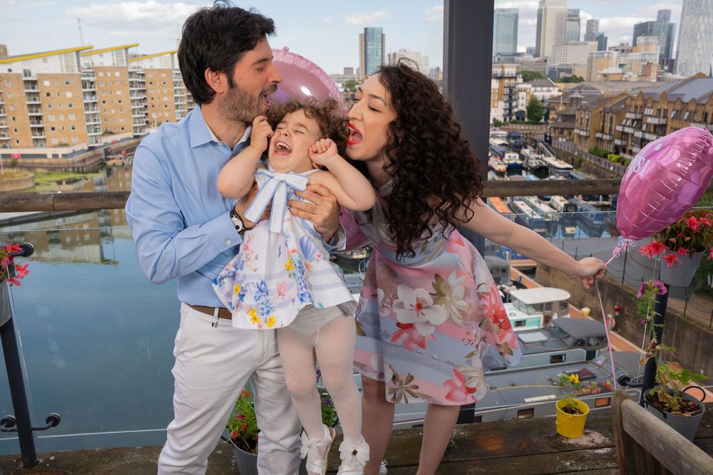 A family shares a tender moment on a balcony overlooking a city skyline with tall buildings in the background.