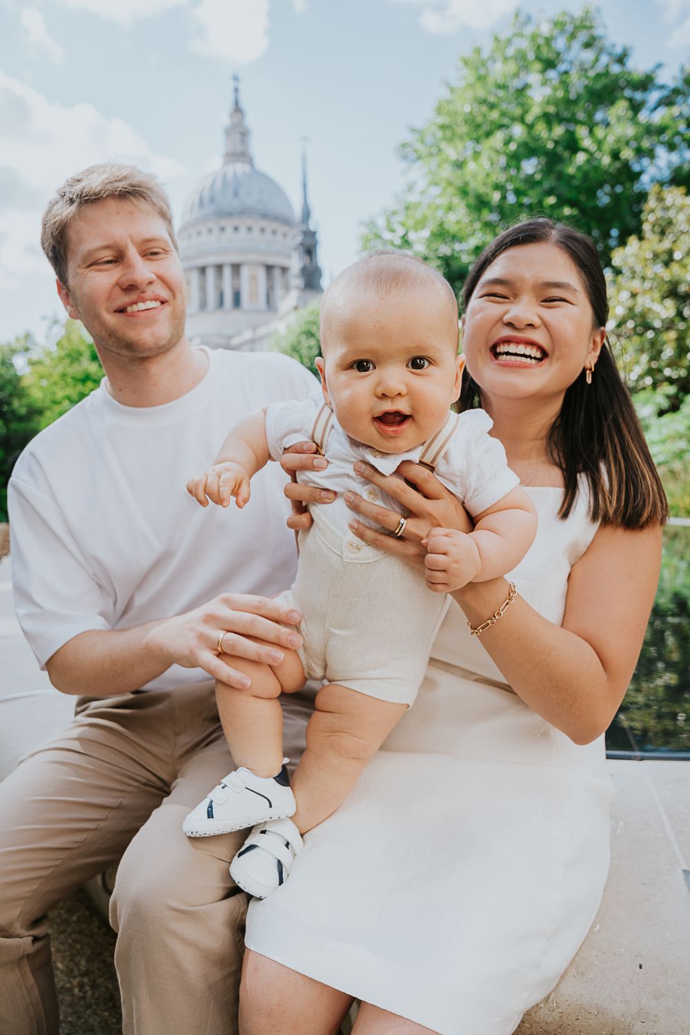 A young family poses together while sitting outdoors near St Paul's Cathedral in London on a sunny day.