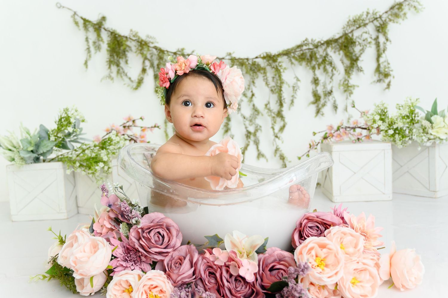 Baby milestone photoshoot with pink and purple floral decorations in white studio setting.