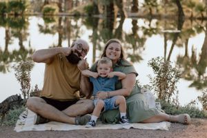 A family sitting by a reflective lake sharing a playful moment together.