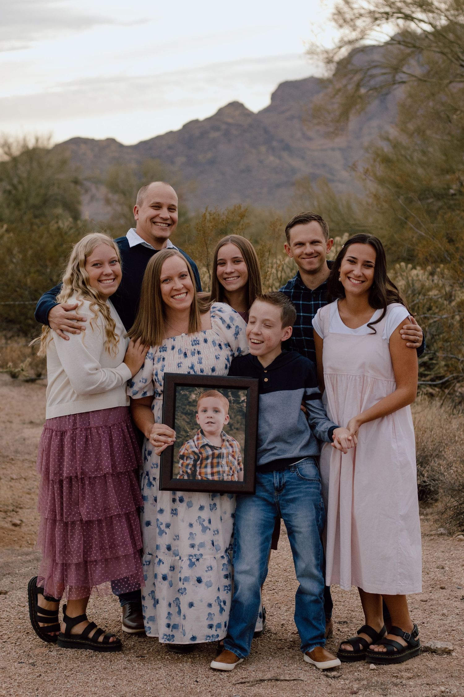 A group poses for a family portrait in the desert with mountains in the background.
