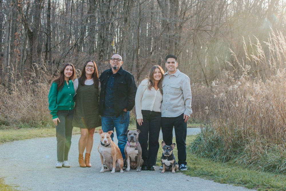 A group of people and dogs pose together on a winding path surrounded by autumn foliage in a natural setting.