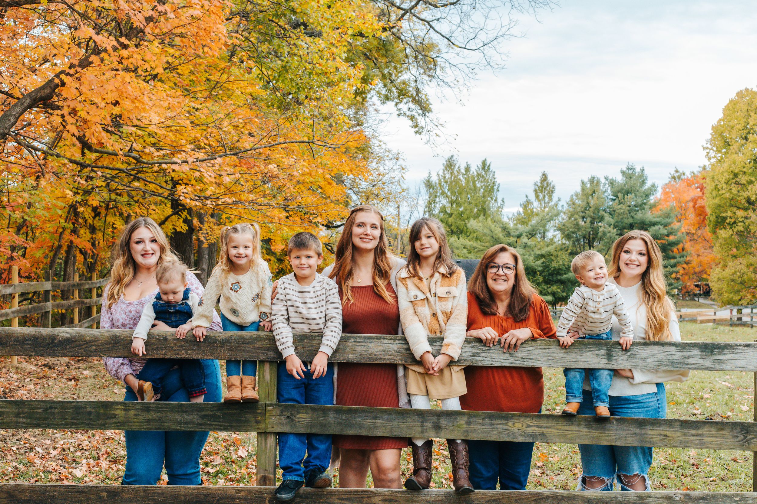 A family leans against a fence under vibrant autumn foliage.