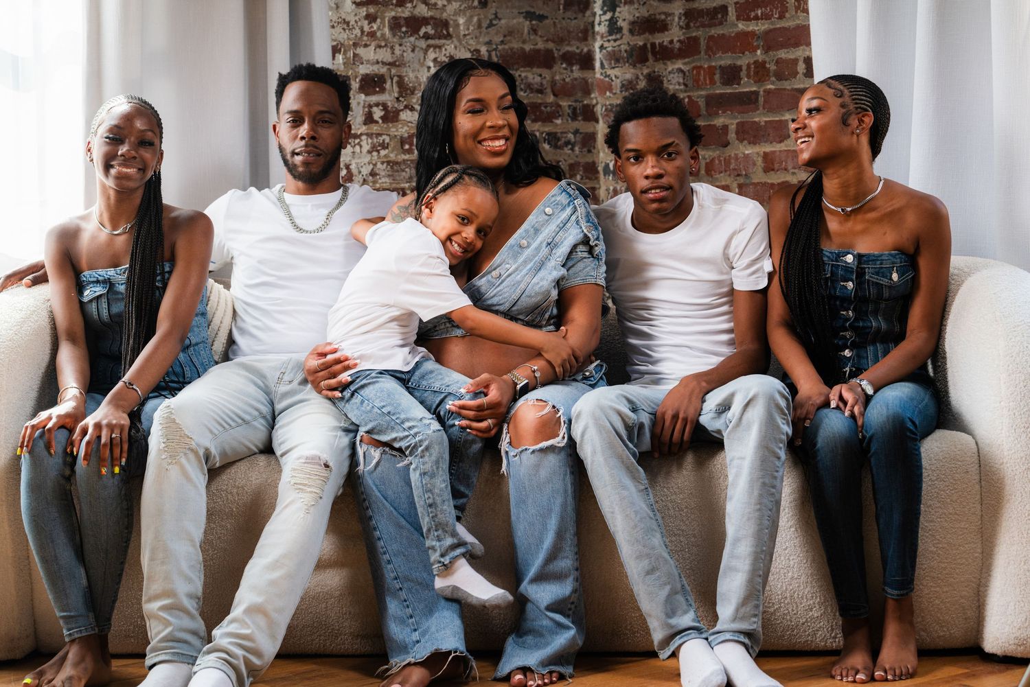 Group lounging together on grey couch in casual wear against brick wall background.