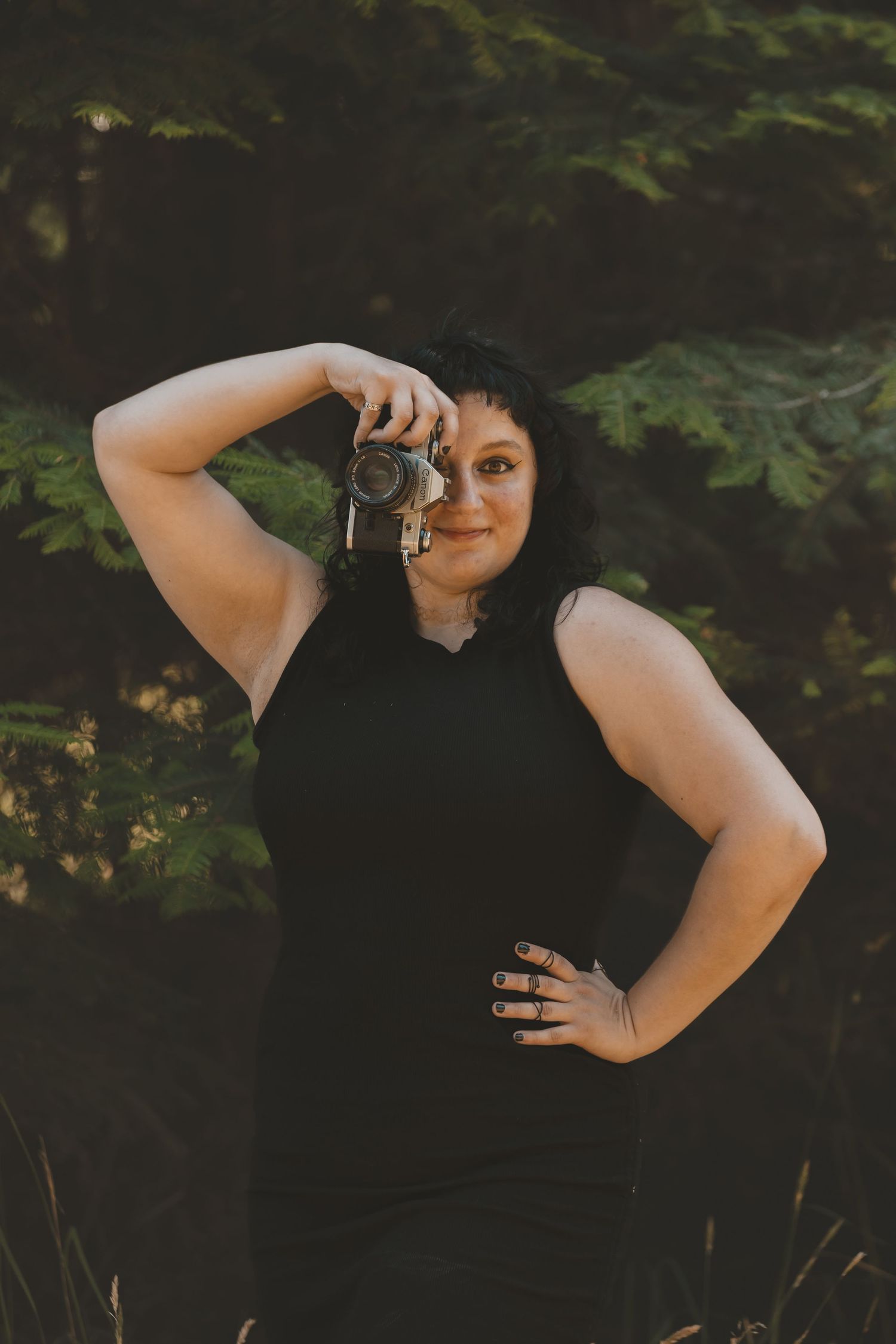 a woman is in front of a tree holding a camera