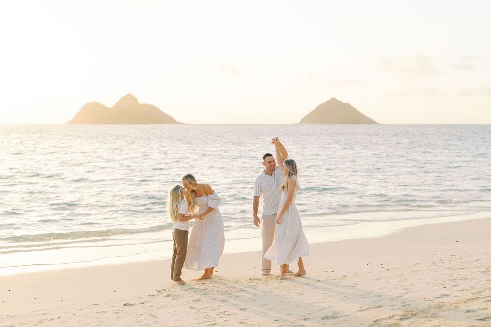 Two couples celebrate on a sandy Hawaiian beach at sunset with twin island peaks visible in the golden ocean backdrop.