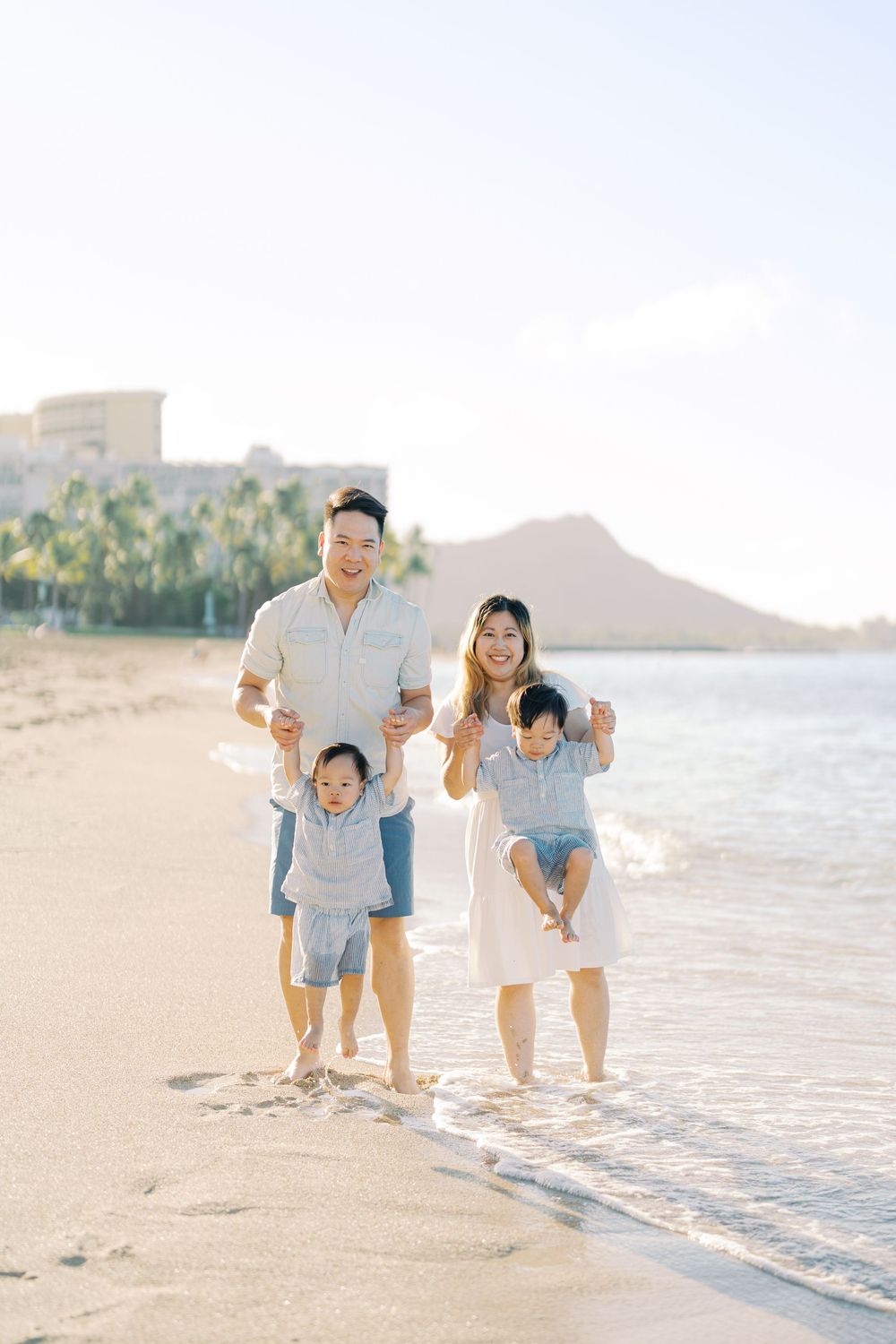 Family of four enjoying a sunny beach walk in Hawaii with Diamond Head crater and palm trees in the background.