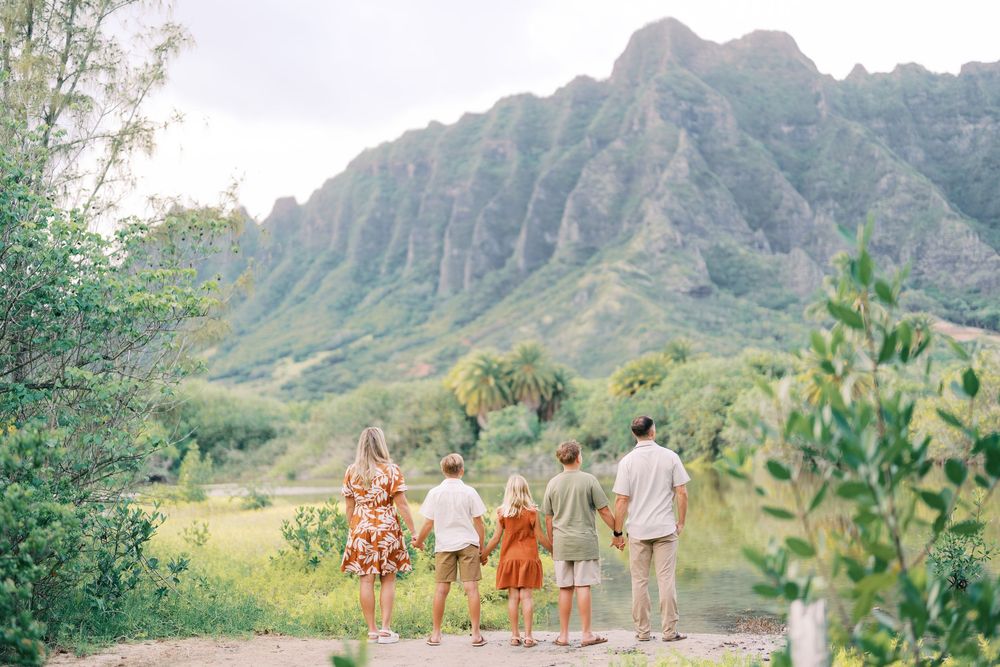 Family of five walking toward lush green mountains in Hawaii, viewed from behind on a scenic tropical path.