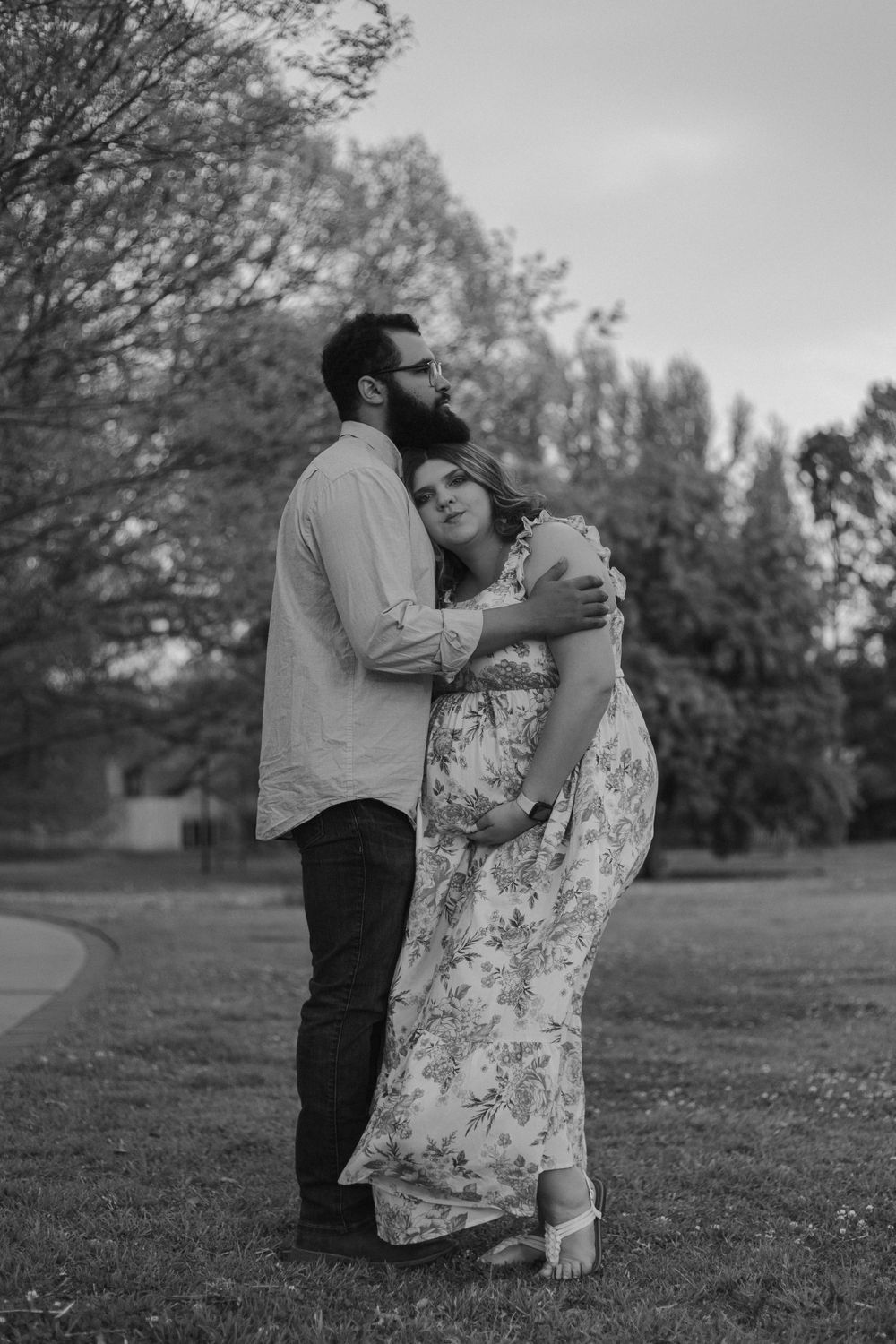 A romantic black and white portrait of a couple embracing outdoors with trees in the background.