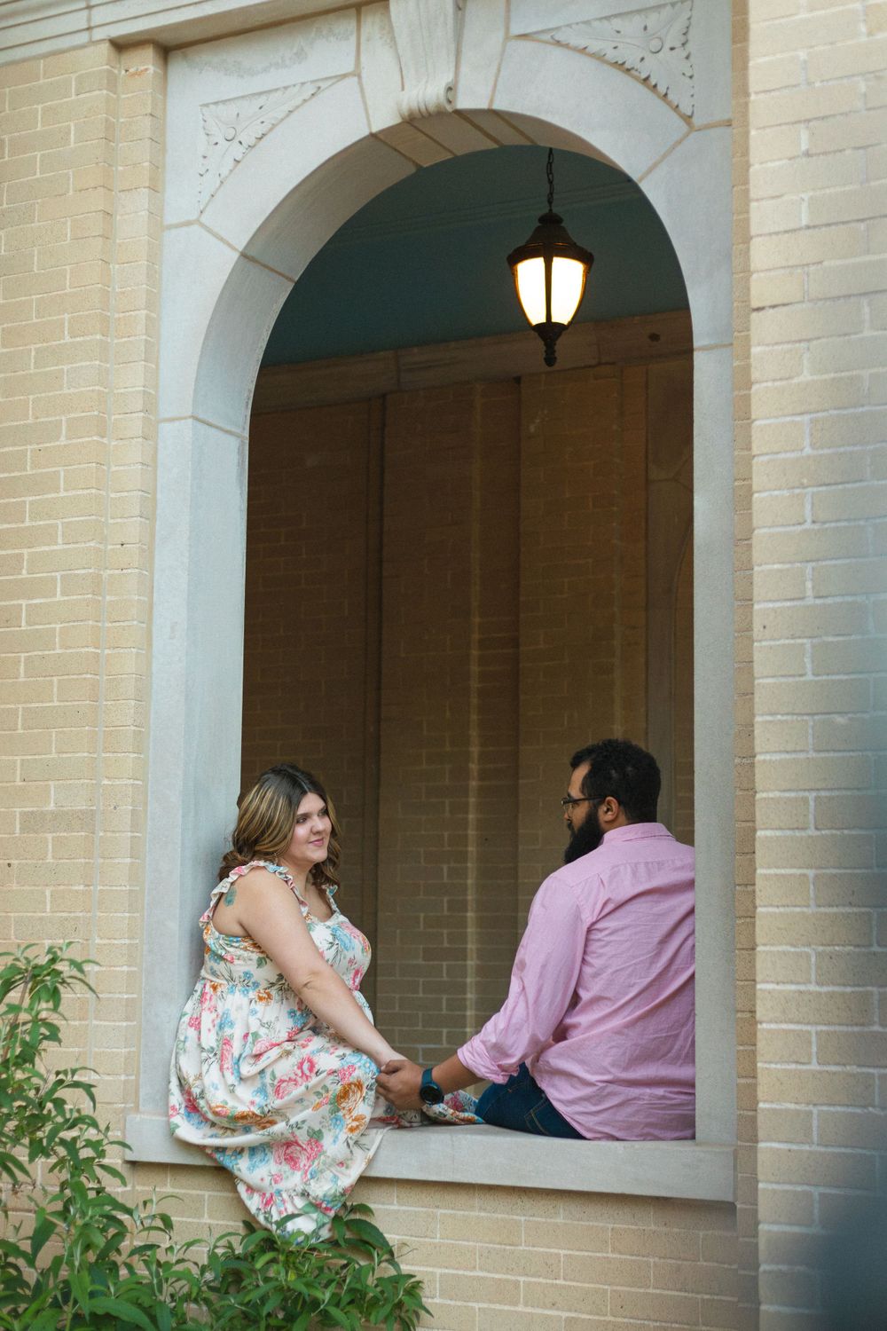 A couple sits together in an arched brick alcove with a hanging lantern overhead.