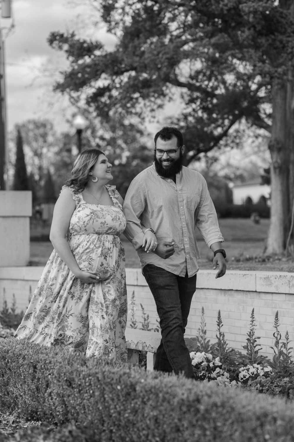 Black and white photo of couple walking together through garden pathway.