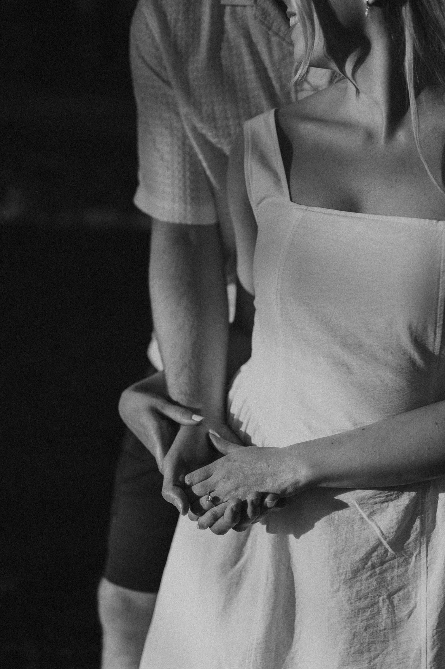 Black and white photo of a couple holding hands, woman in white dress with man behind her.