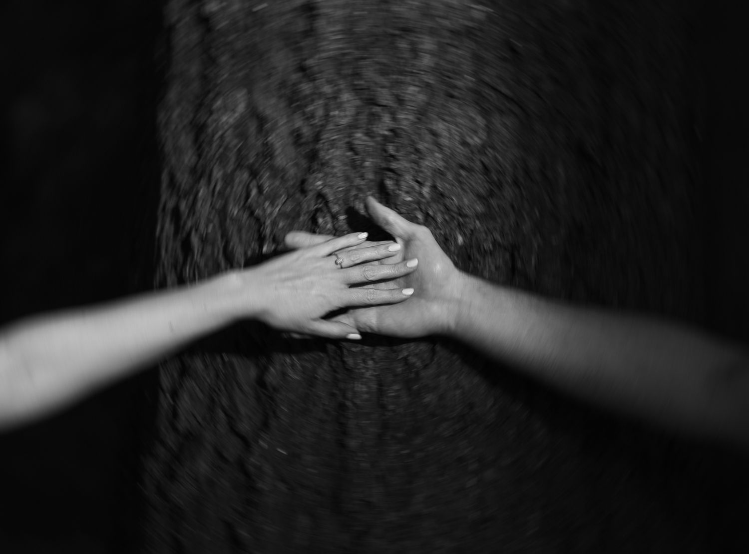 Two hands gently resting on a dark textured surface in a tender black and white photograph.