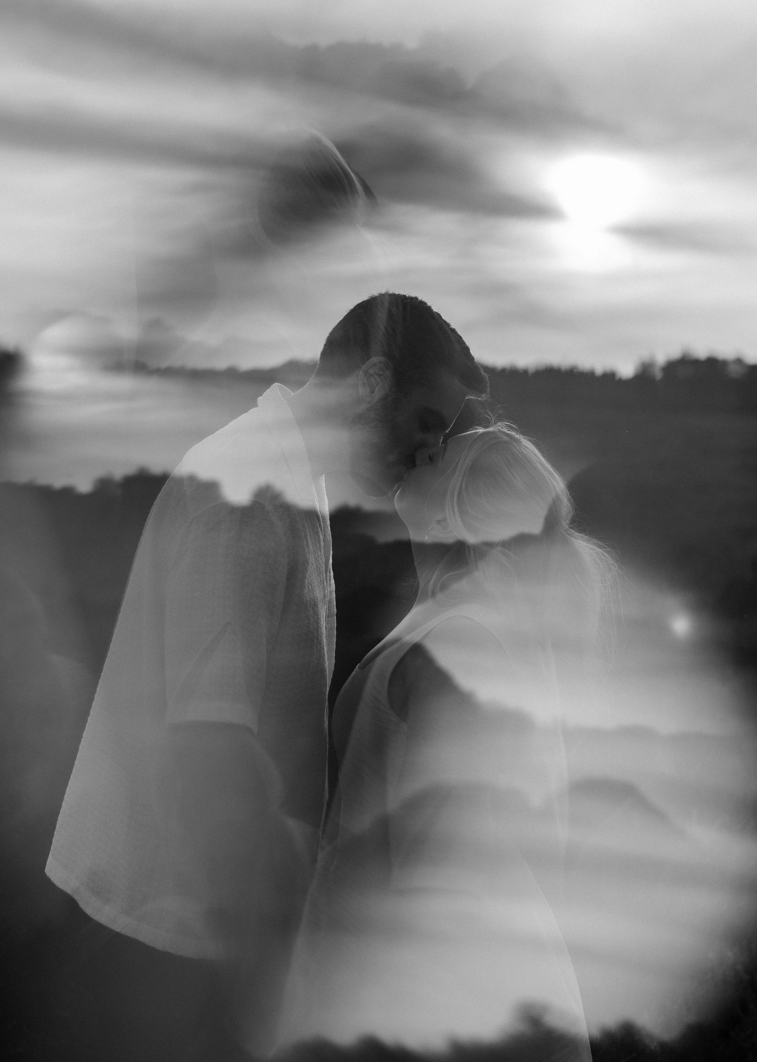 Black and white double exposure photo of a person in white shirt against dramatic cloudy sky.