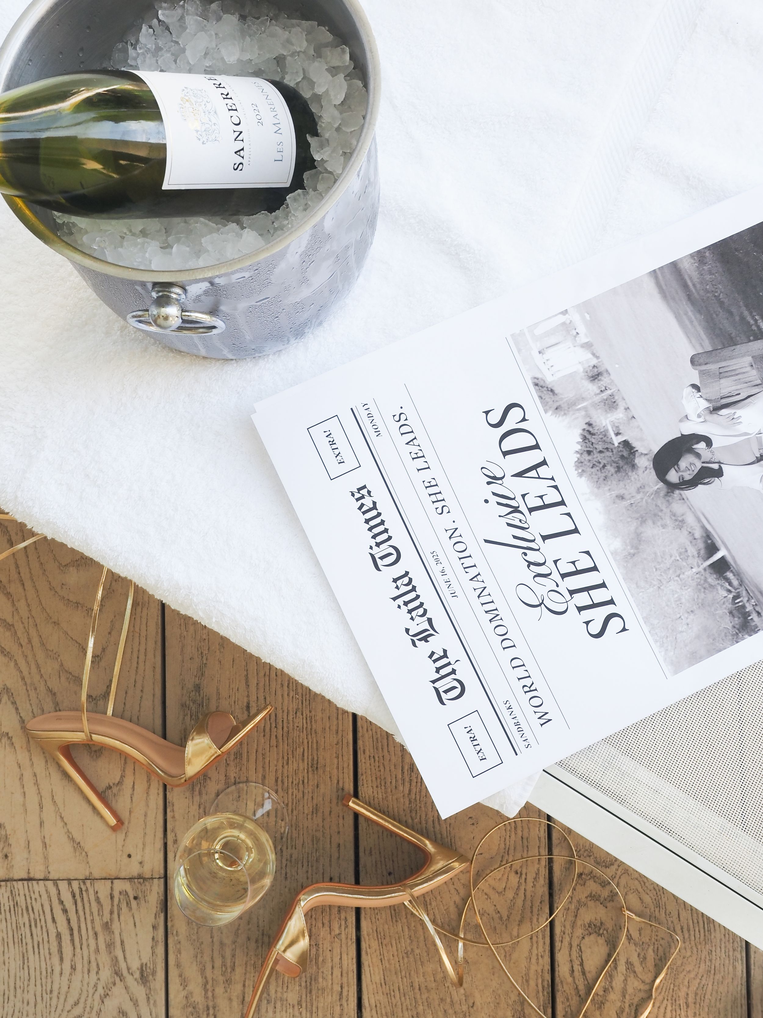 Wine bottle in ice bucket with event invitation and copper decorations on wooden floor.