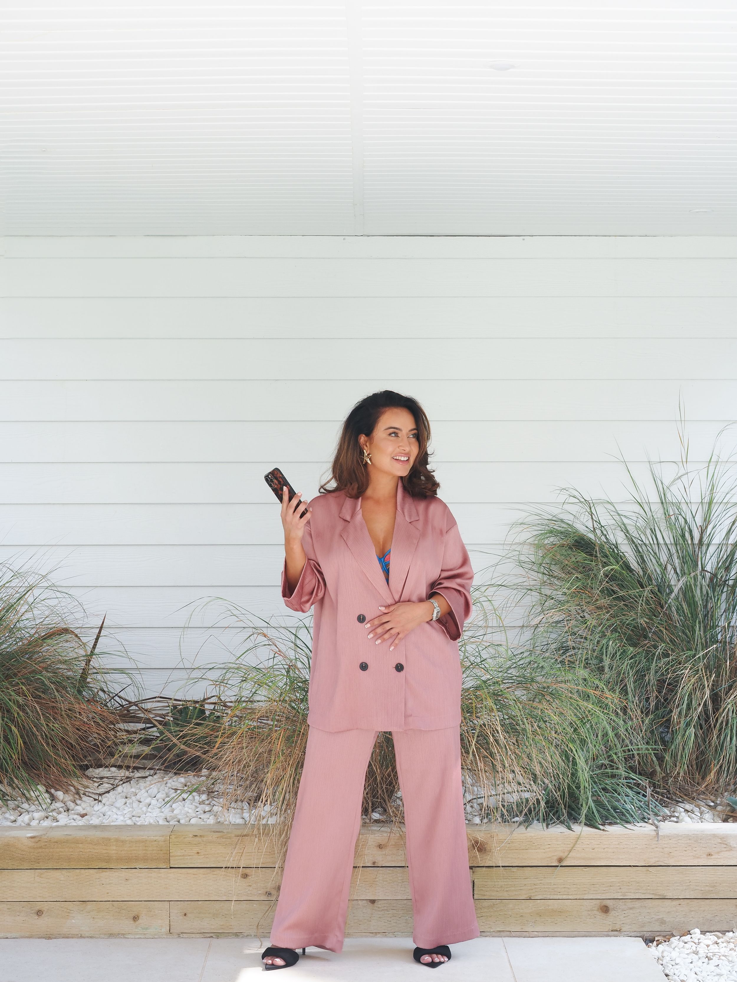 Person in oversized pink suit lounging on white porch with beach grass in background.