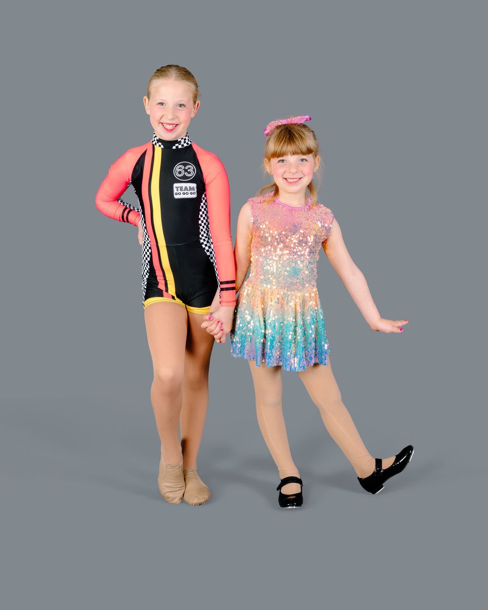 Two dancers in colorful performance attire strike dynamic poses against a gray studio backdrop.