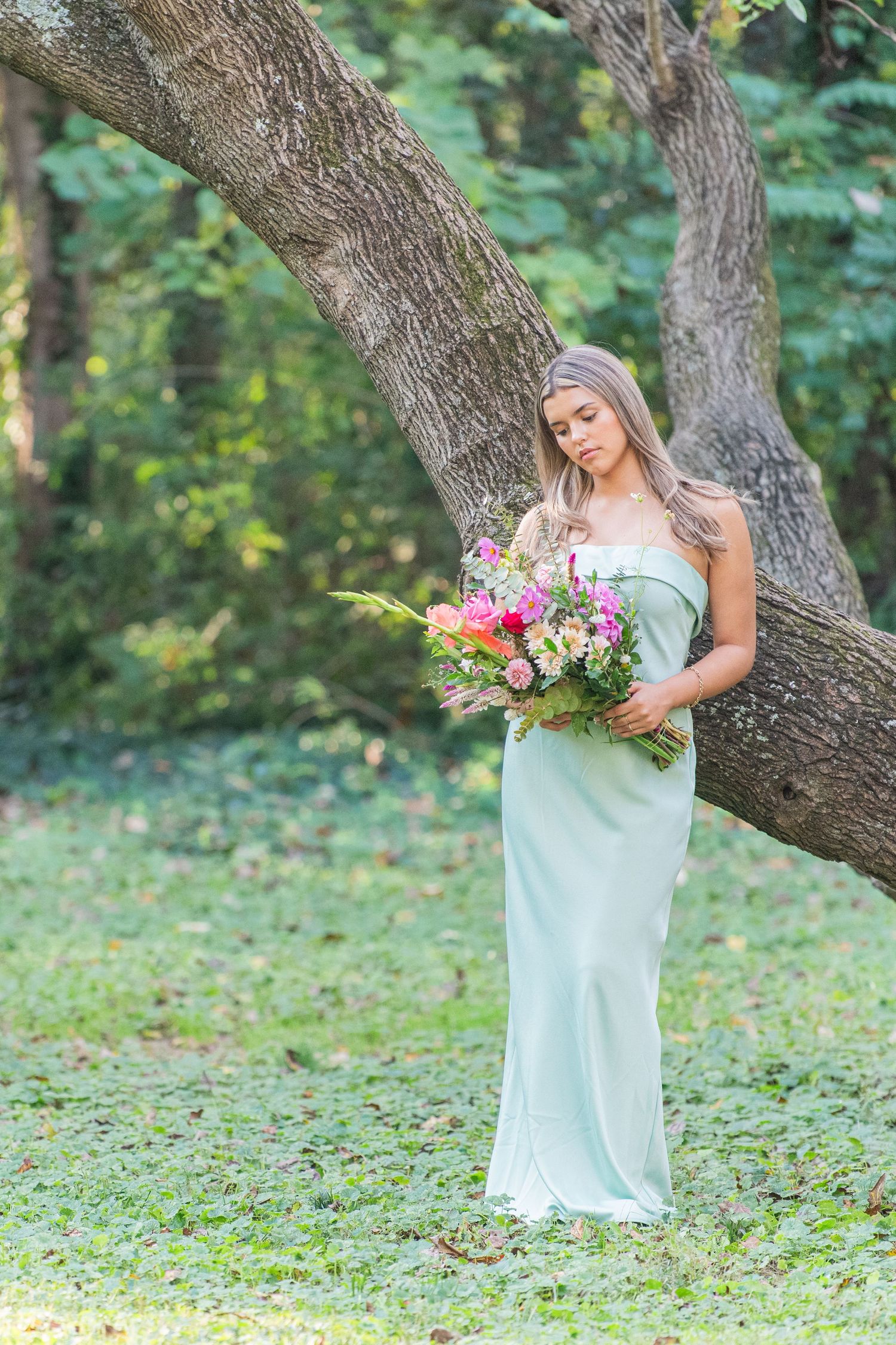 Beautiful young woman celebrating her quinceañera, holding a bucket of wildflowers in a pretty green light dress, surrounded by nature.