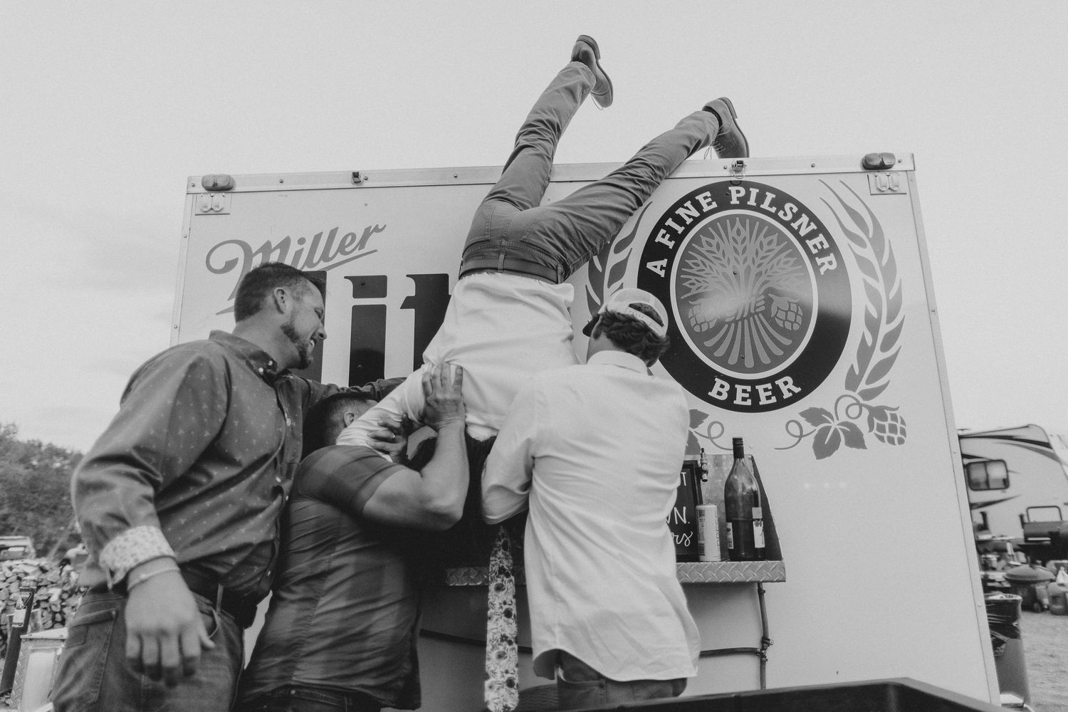 Groom doing a keg stand with the help of his friends.