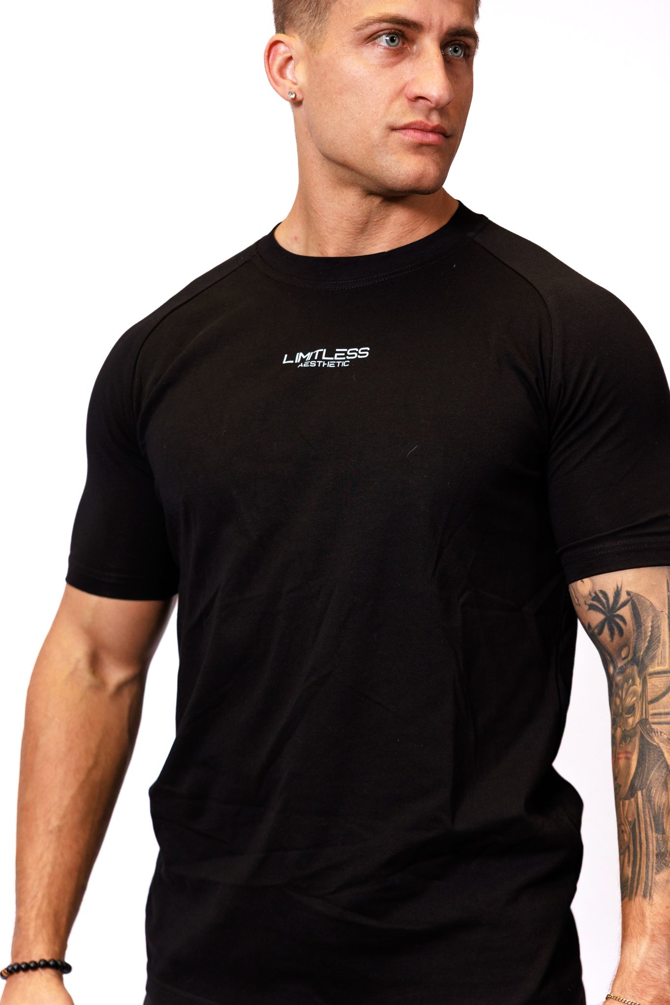Athletic man in black t-shirt showing tattoo sleeve on arm against white background.