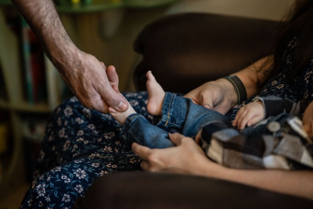 Close-up of an elderly hand and a younger hand gently holding a newborn baby's feet and legs.