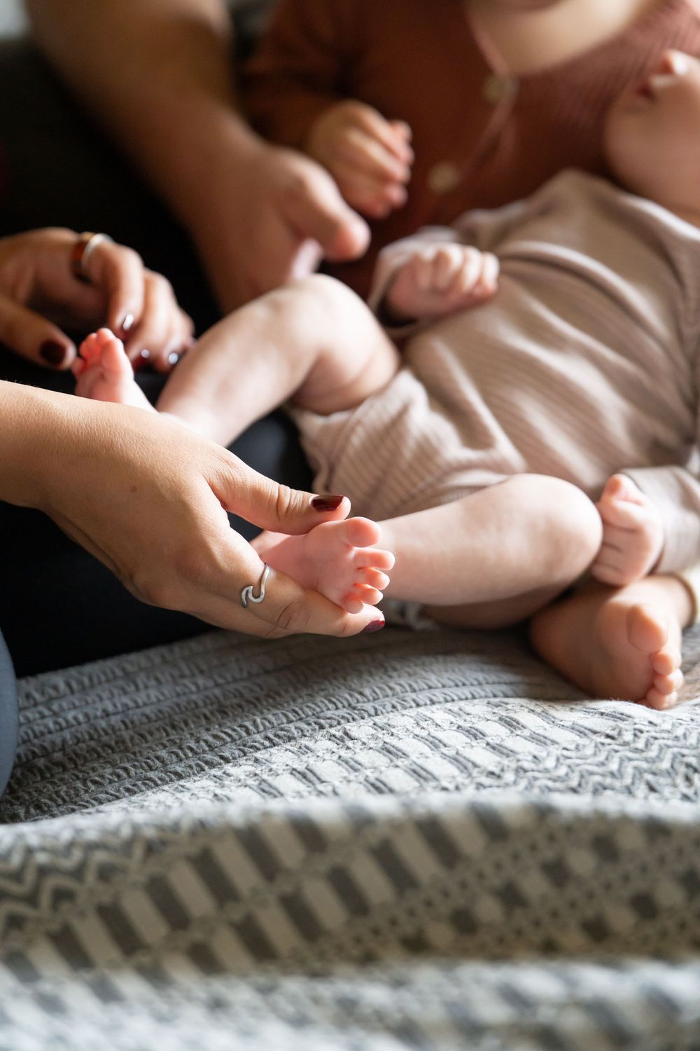 Adult hands gently holding tiny newborn baby feet on a soft knit blanket, capturing a tender family bonding moment. lifestyle session