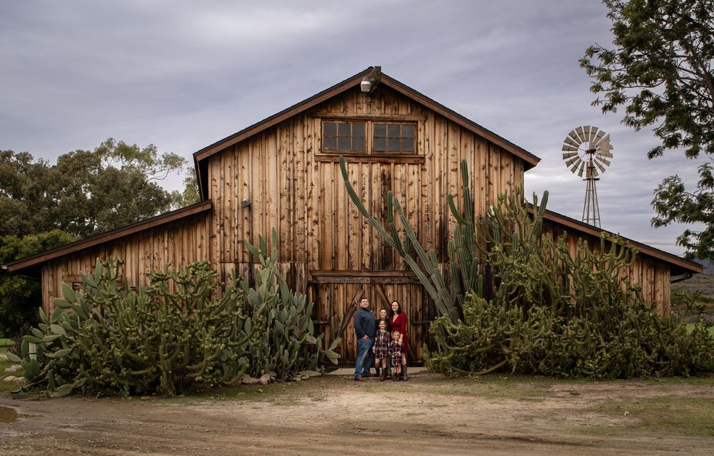 Family posing in front of a rustic wooden barn surrounded by cacti with a windmill in the background.
