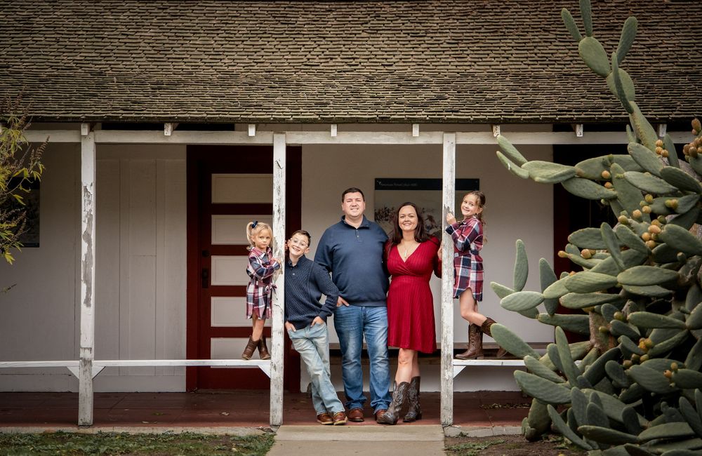 Happy family of four posing on front porch of home with cactus nearby on a sunny day.