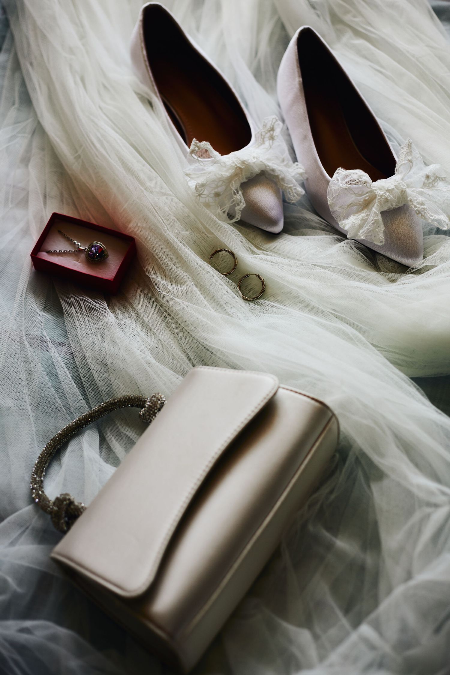 Wedding accessories including white shoes, purse, and jewelry arranged on tulle fabric.