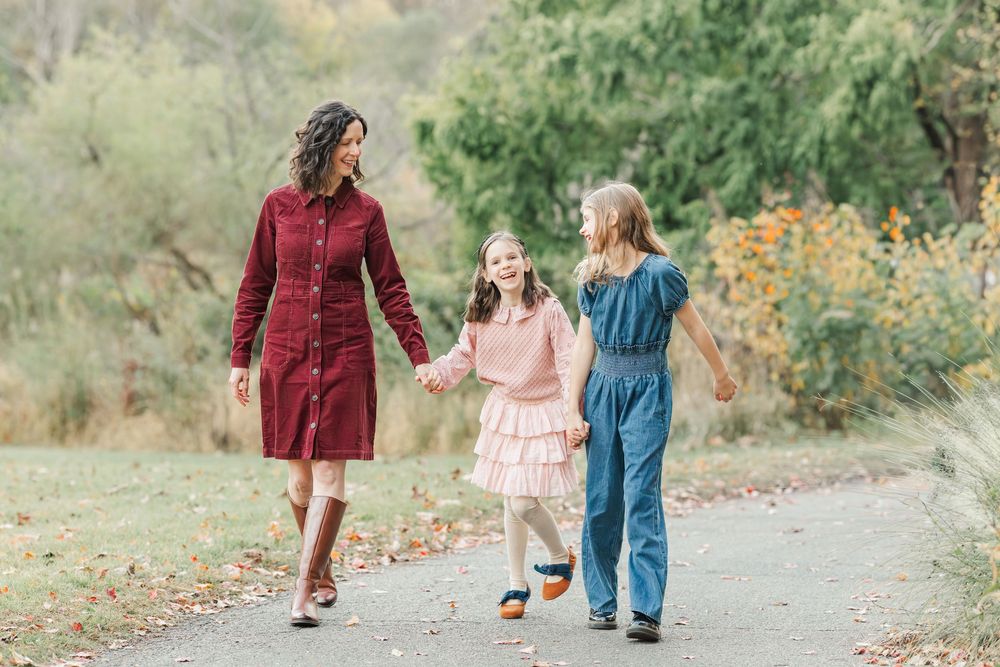 A family walks together holding hands along a winding autumn path through nature.
