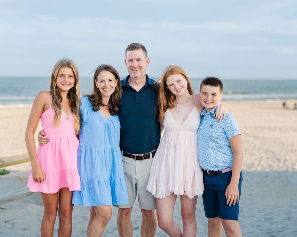 A family poses together on a sunny beach wearing pastel colors and summer attire.