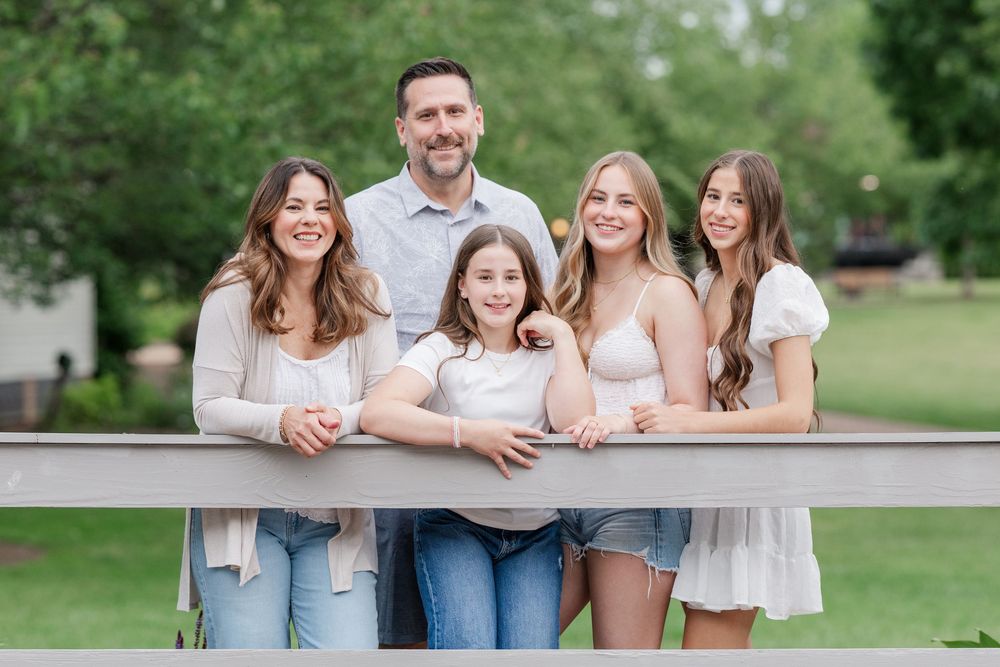 Family in coordinating outfits smiling while leaning on fence outdoors in park setting at Vienna VA Centennial Park