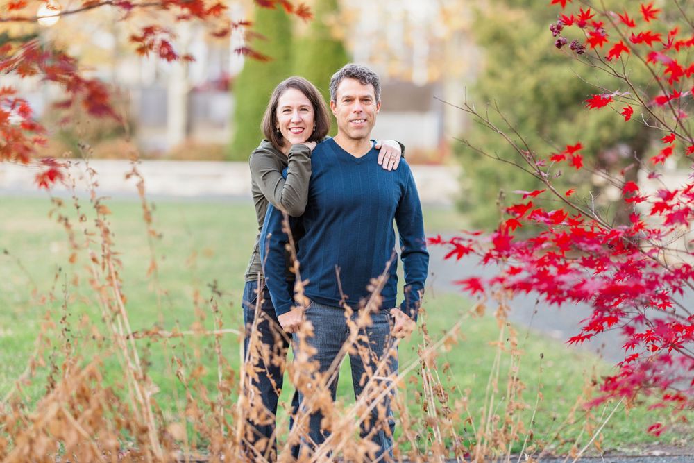 A couple poses outdoors in autumn surrounded by vibrant red maple leaves and fall foliage.