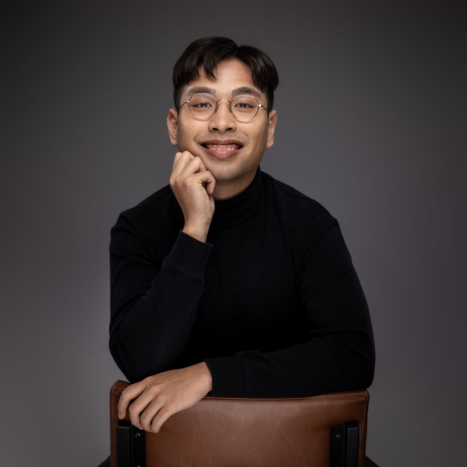 Portrait of person in black turtleneck and glasses posing against dark background.