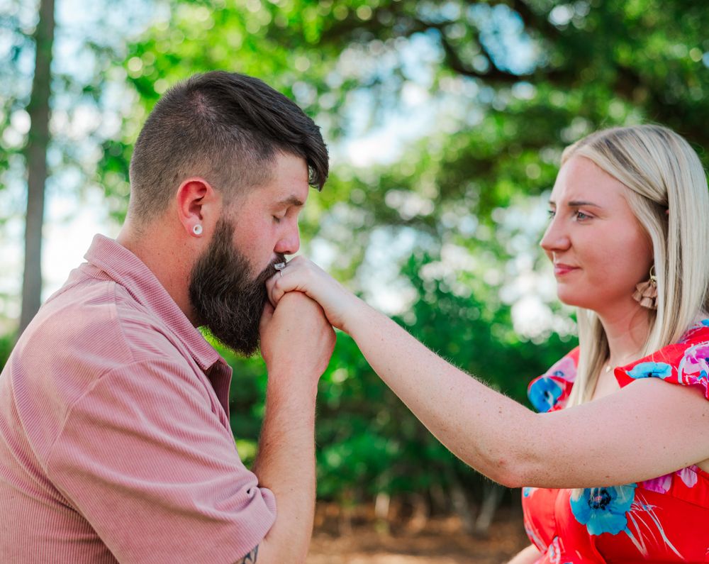 A romantic moment captured as a bearded man kisses his partner's hand outdoors.