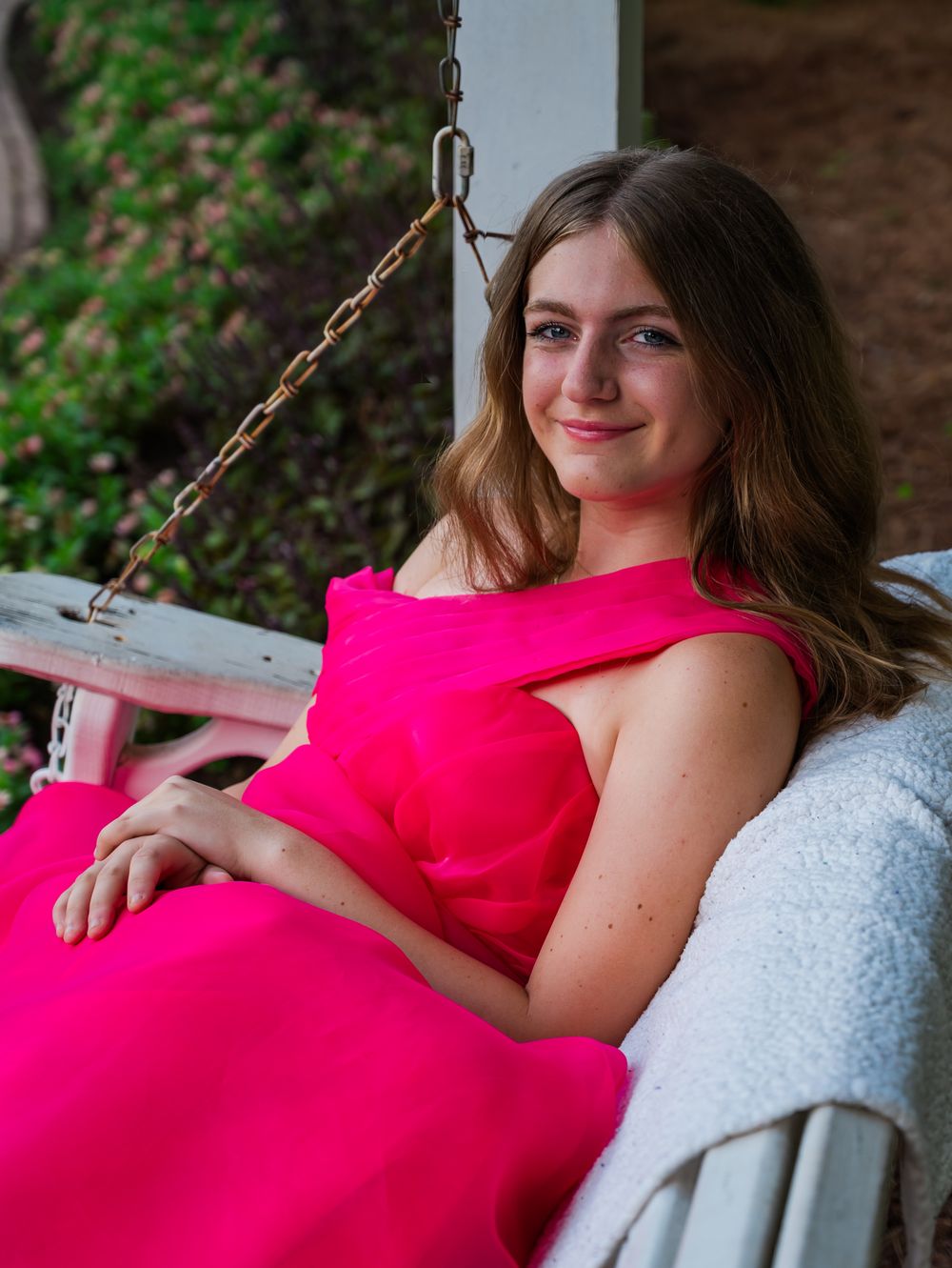Elegant portrait in a vibrant pink dress while sitting on a porch swing.