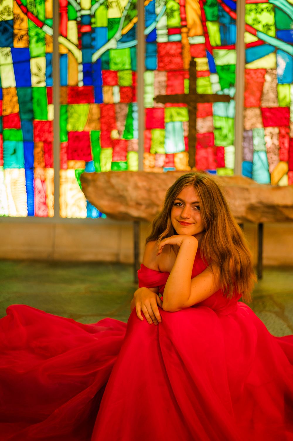 Dramatic portrait against colorful stained glass background in flowing red gown.