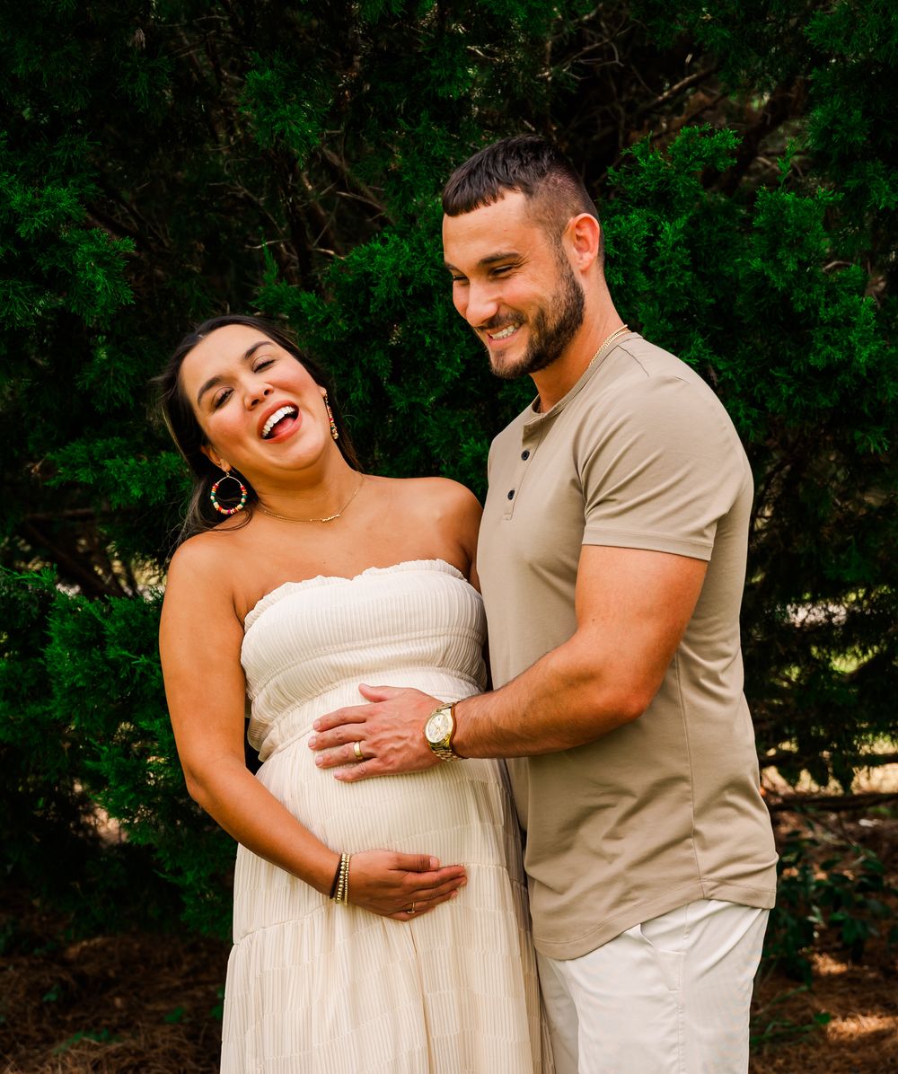 Joyful couple sharing a tender moment during maternity photoshoot outdoors.