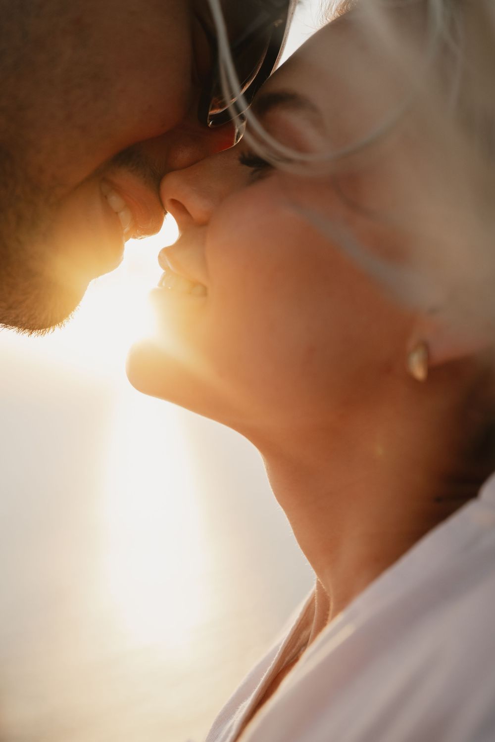 Romantic couple sharing a tender moment at golden sunset, faces close together in a warm glowing backlit embrace.
