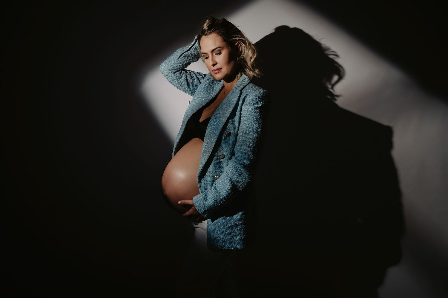 Silhouetted side profile of pregnant woman in black dress against grey background.