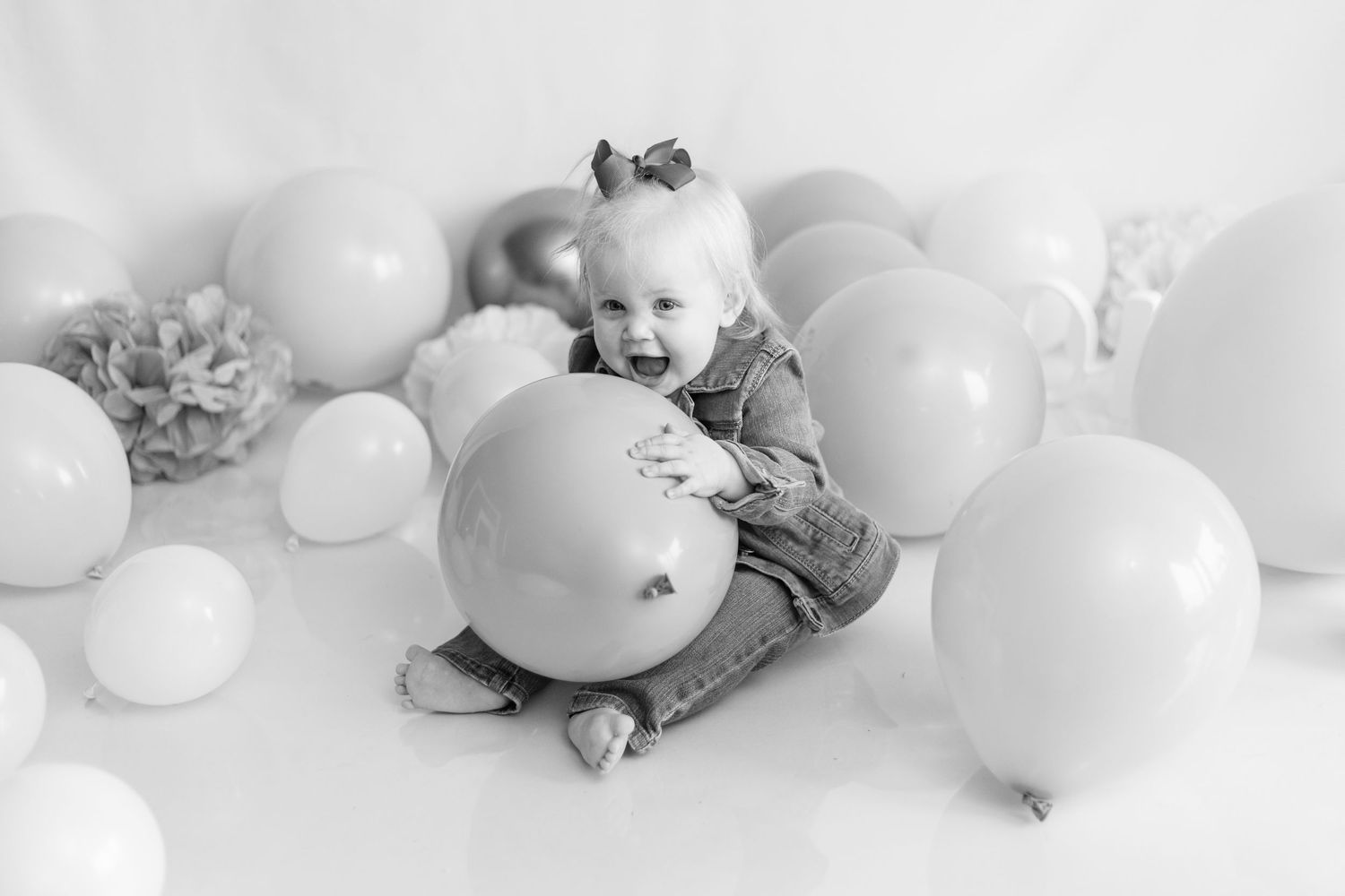 A small child plays among pink and purple balloons in a festive setting.