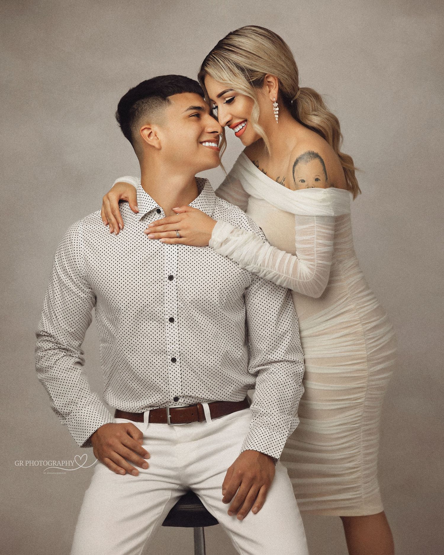 A couple embraces tenderly while wearing coordinated white and cream outfits in a romantic studio photoshoot.