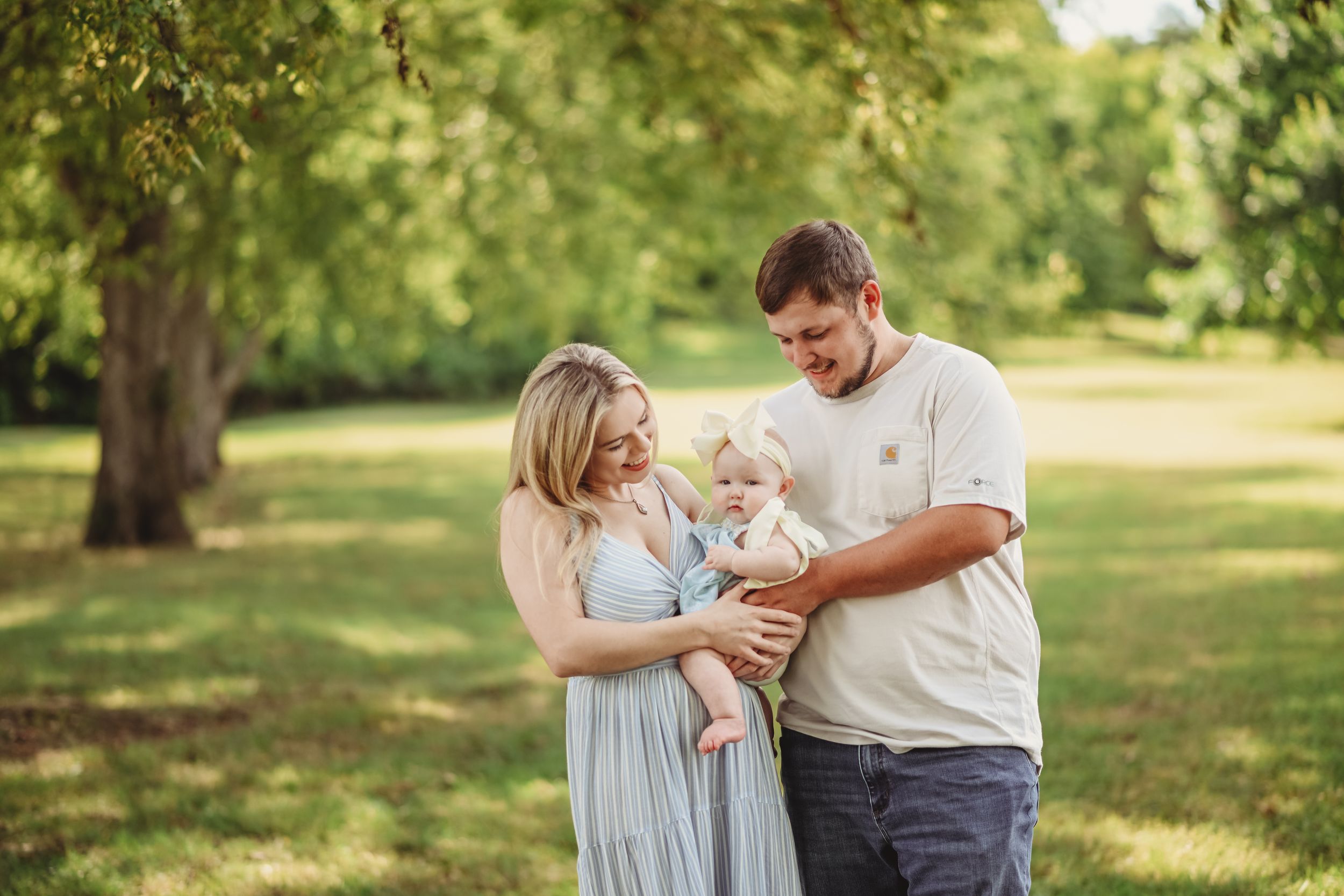 Couple shares tender moment during outdoor maternity photo session in park.