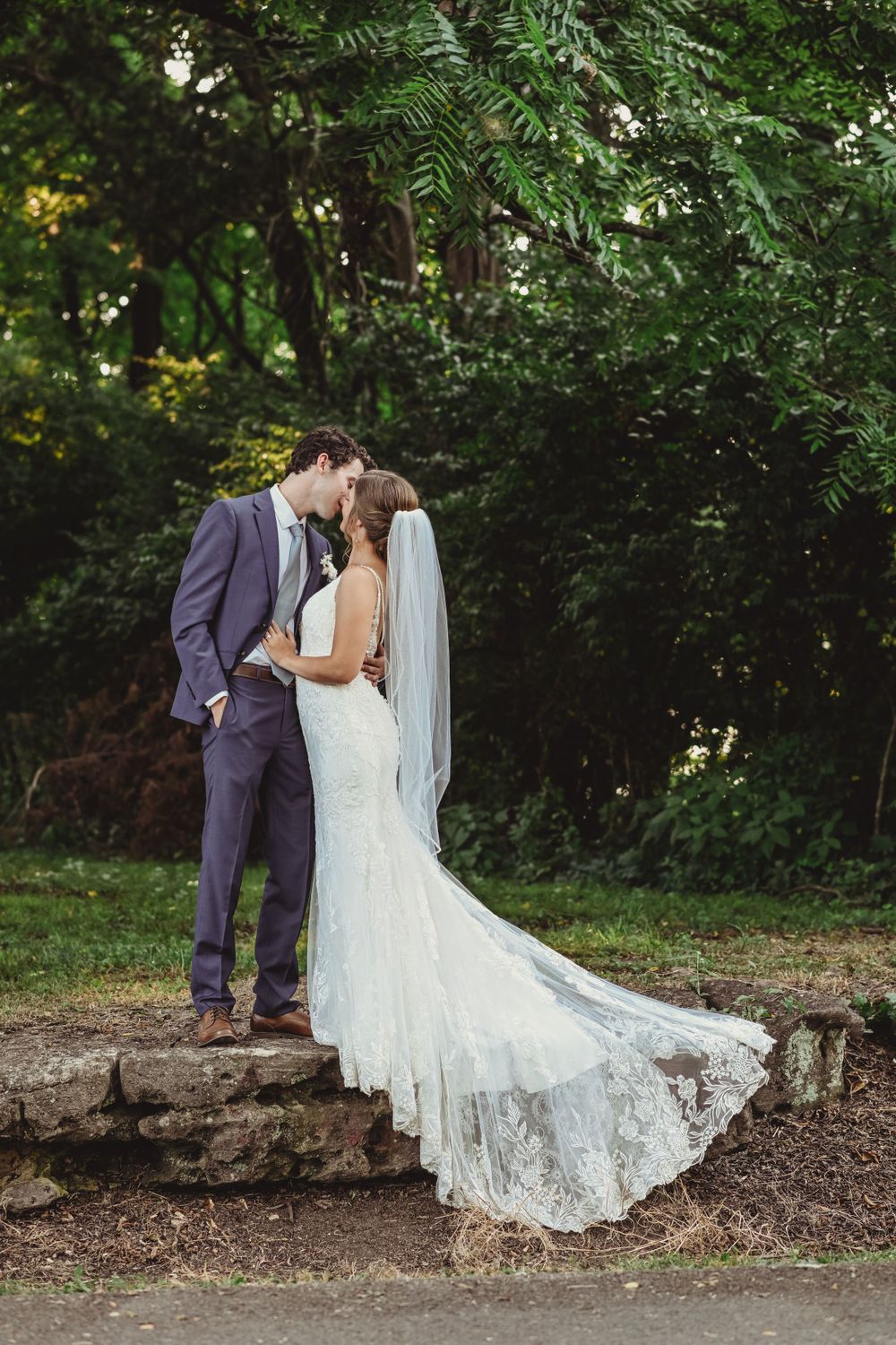 Couple shares an intimate moment on stone steps surrounded by lush greenery.