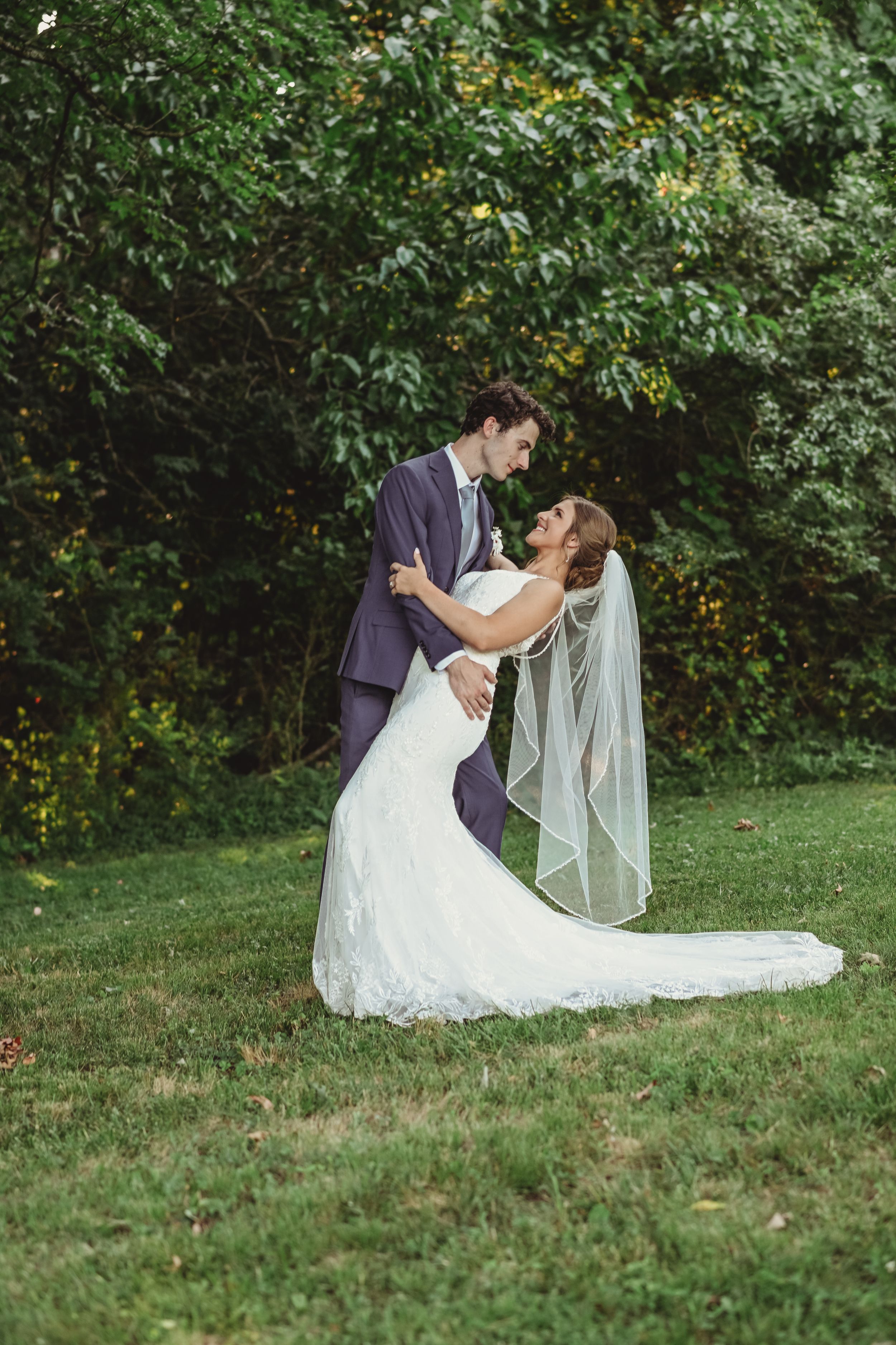 Bride and groom embrace on a grassy hillside during their outdoor wedding.