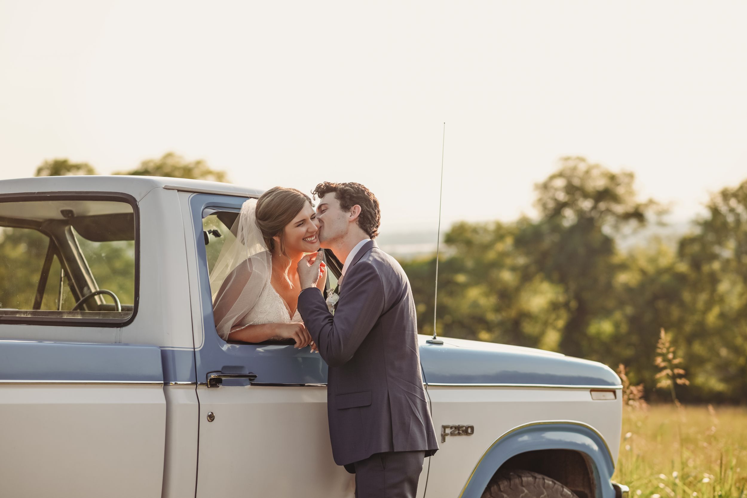 Couple embraces near vintage truck during golden hour wedding photography.