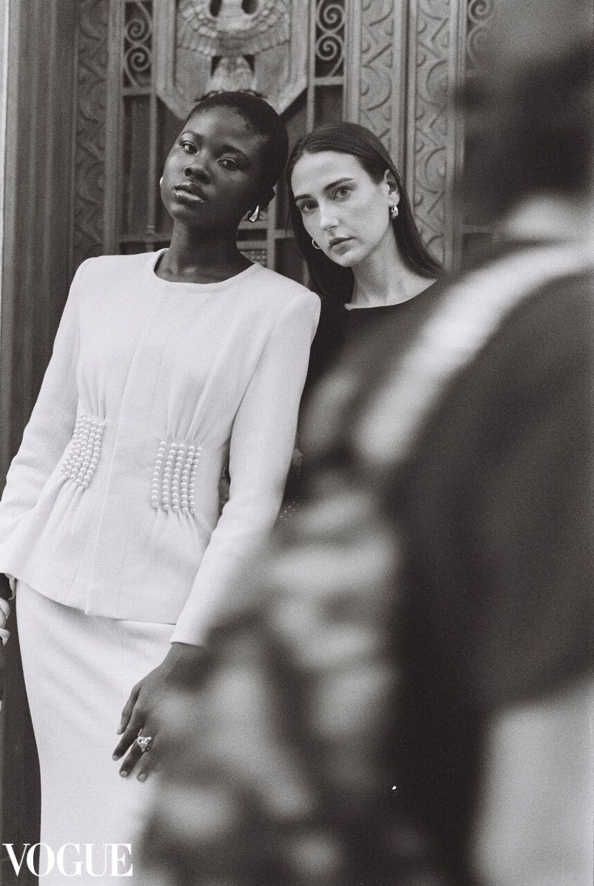 Black and white Vogue fashion photograph showing elegant models in white clothing against an ornate backdrop.
