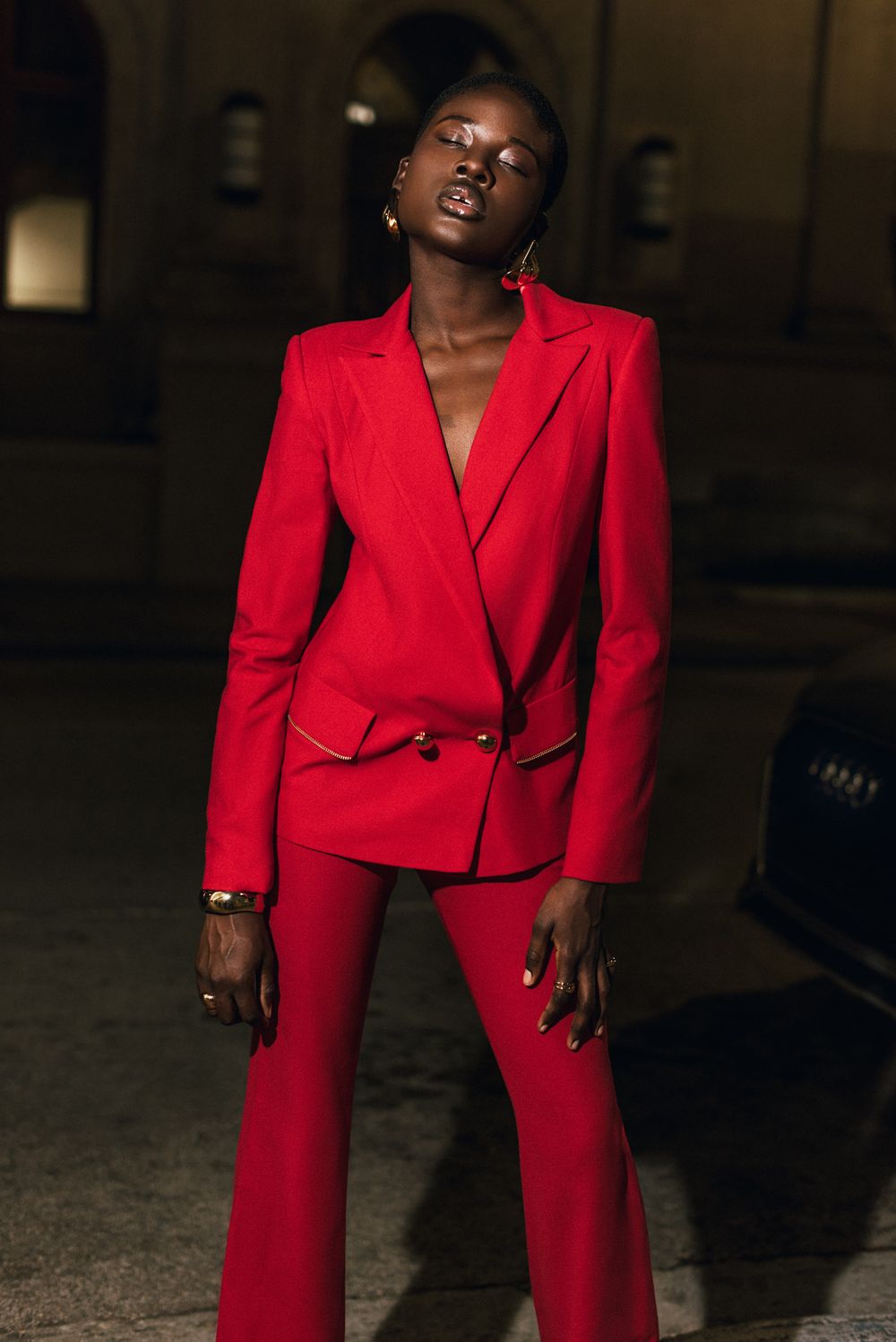 An elegant red power suit with a tailored blazer and matching pants photographed against a dark background.