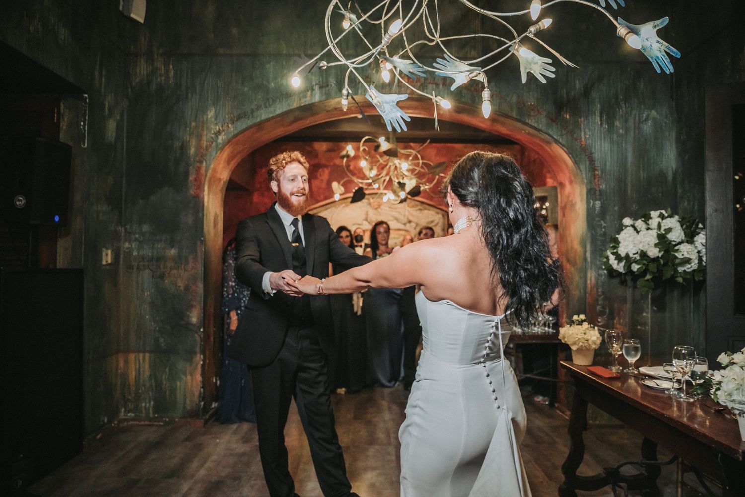 Couple dancing in an intimate venue with string lights and rustic decor.